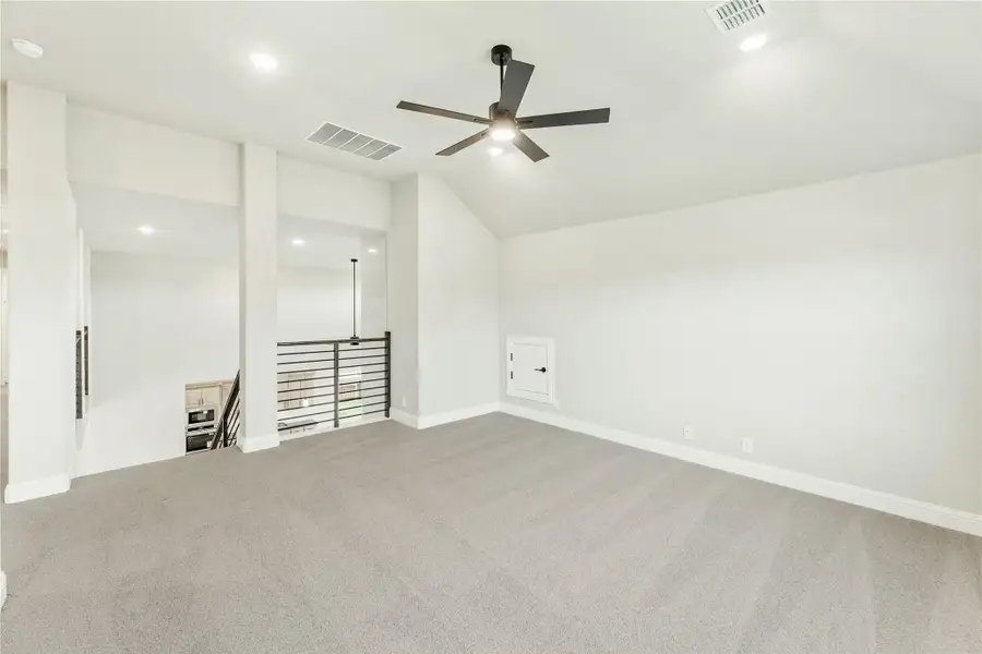 Empty room with vaulted ceiling, ceiling fan, gray carpet, and open stair railing visible in background Empty room with vaulted ceiling, ceiling fan, gray carpet, and open stair railing visible in background