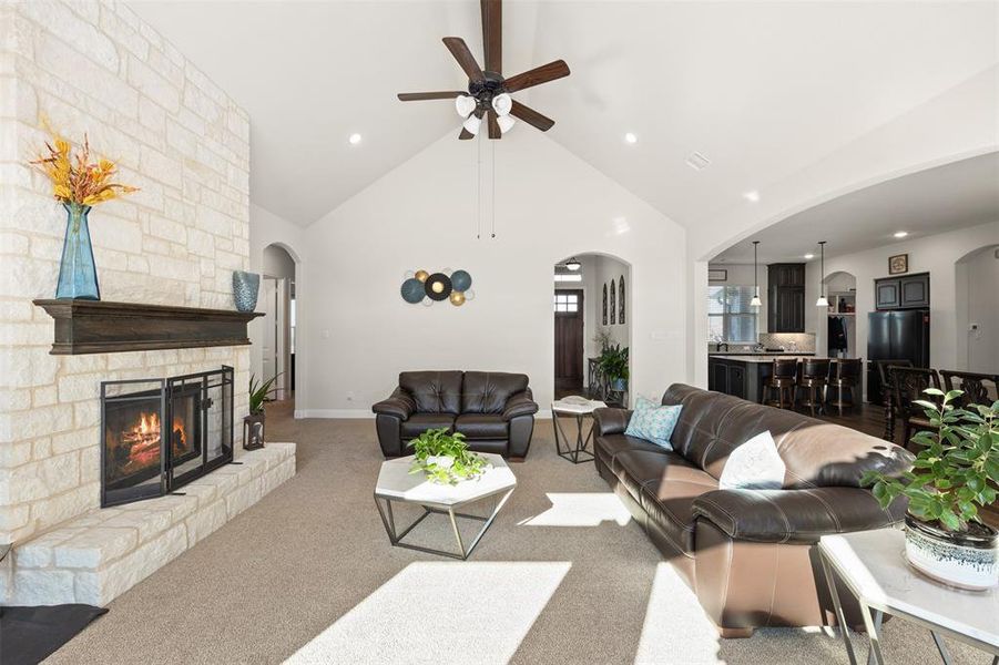 Living room with ceiling fan, light colored carpet, vaulted ceiling, and a fireplace Living room with ceiling fan, light colored carpet, vaulted ceiling, and a fireplace
