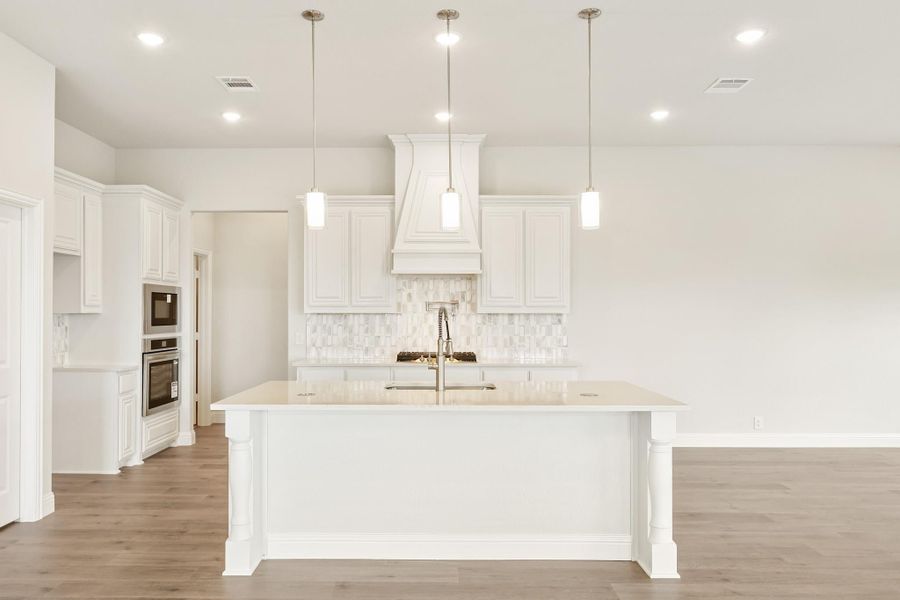 White kitchen with large island, pendant lights, tile backsplash, and stainless steel double ovens