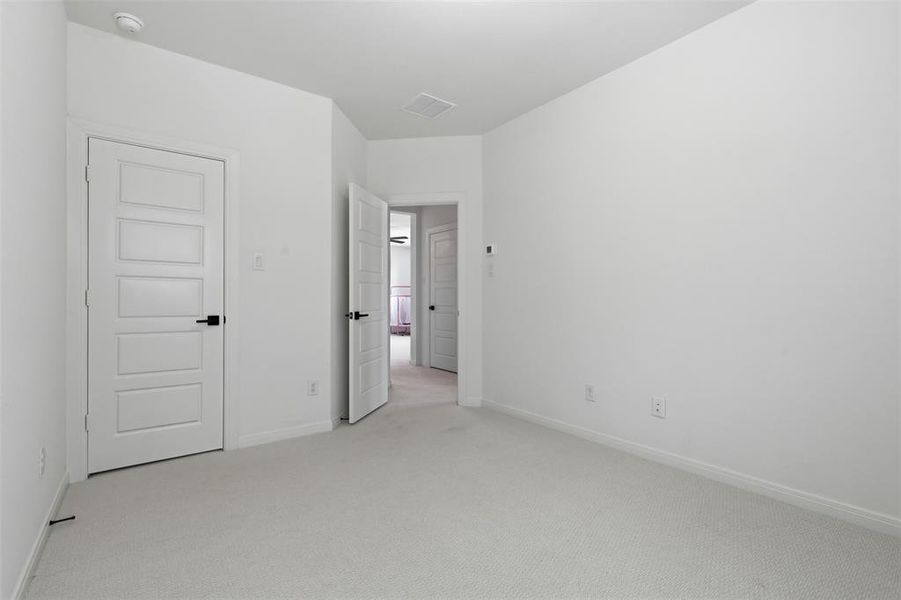 Spacious room with new carpet, crisp white walls, and a five-panel interior door with matte black hardware Spacious room with new carpet, crisp white walls, and a five-panel interior door with matte black hardware