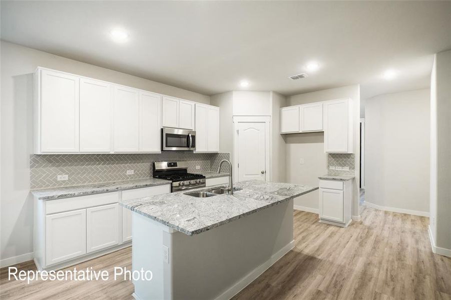 Kitchen with white cabinetry, a center island with sink, stainless steel appliances, and light hardwood / wood-style flooring