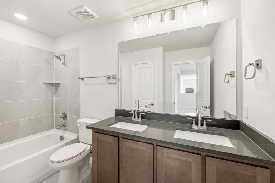 Bathroom with double sink vanity, dark countertop, tub-shower combo, and large mirror with overhead lighting Bathroom with double sink vanity, dark countertop, tub-shower combo, and large mirror with overhead lighting