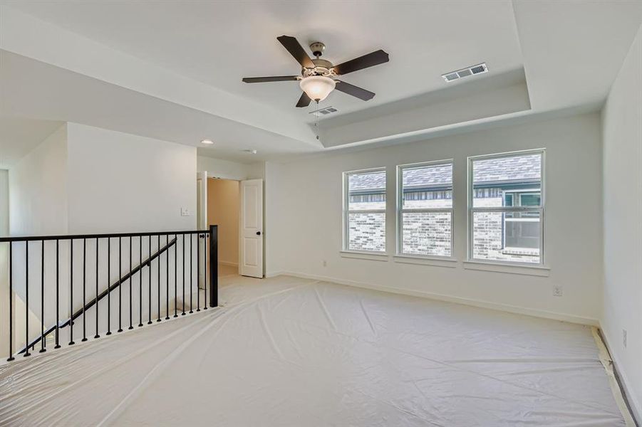 Unfurnished room featuring light carpet, a tray ceiling, and a ceiling fan Unfurnished room featuring light carpet, a tray ceiling, and a ceiling fan