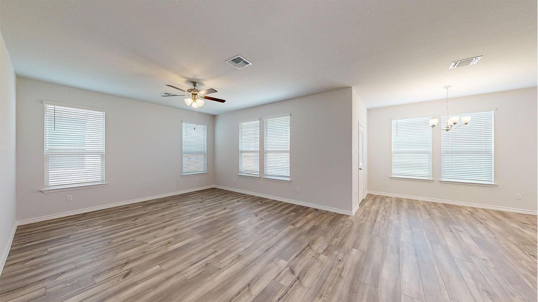 Spacious room featuring wood-finish flooring, light-colored walls, multiple windows with blinds, a ceiling fan with light fixture, and an additional chandelier Spacious room featuring wood-finish flooring, light-colored walls, multiple windows with blinds, a ceiling fan with light fixture, and an additional chandelier