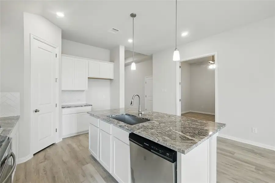 Kitchen with stainless steel dishwasher, a sink, light wood-style flooring, tasteful backsplash, and white cabinetry
