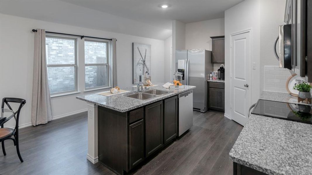 Kitchen featuring a central island with dual sinks, granite countertops, wood-finish flooring, dark cabinetry, and integrated stainless steel appliances Kitchen featuring a central island with dual sinks, granite countertops, wood-finish flooring, dark cabinetry, and integrated stainless steel appliances