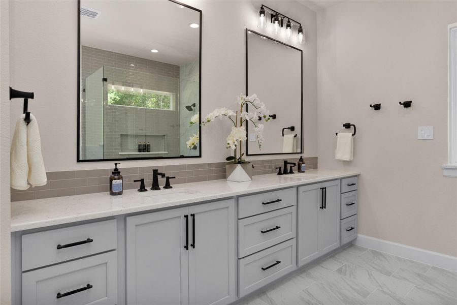 This beautifully designed double vanity features quartz countertops, matte black finishes and framed mirrors with overhead lighting with designer fixtures.