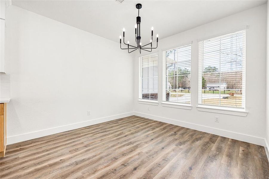 Bright dining area with large windows, modern chandelier, and wood-look flooring, offering a view of the outdoors.