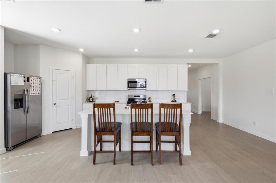 Bright kitchen featuring a central island with seating, white cabinetry, stainless steel appliances, and a subway tile backsplash Bright kitchen featuring a central island with seating, white cabinetry, stainless steel appliances, and a subway tile backsplash