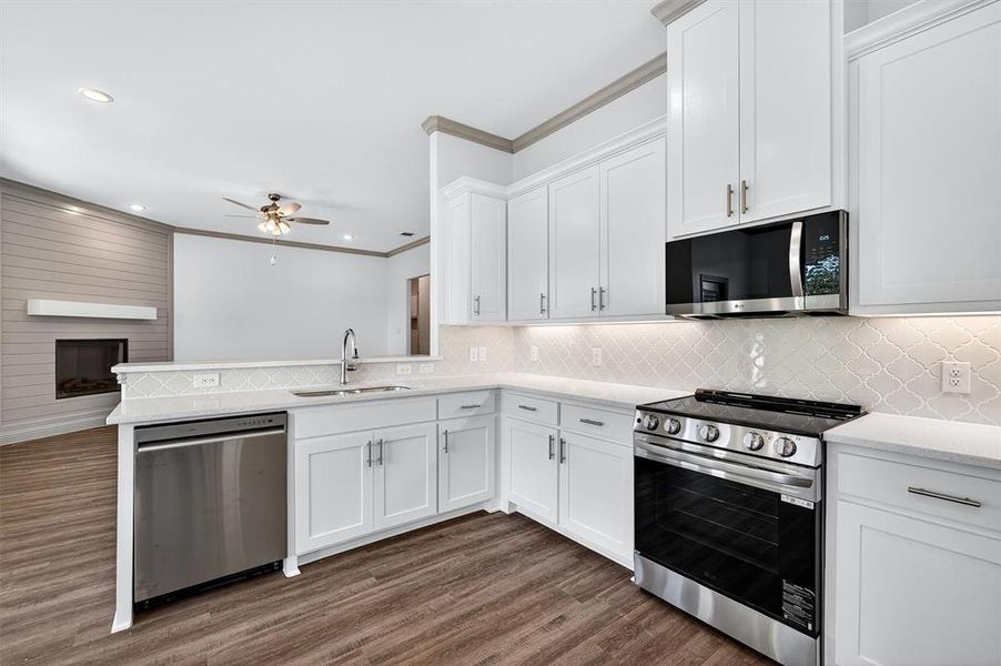 Kitchen with appliances with stainless steel finishes, white cabinets, crown molding, dark wood-style floors, and light stone countertops