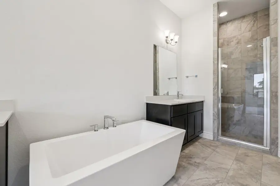 Full bath with vanity, a freestanding bath, a shower stall, and light marble finish floors