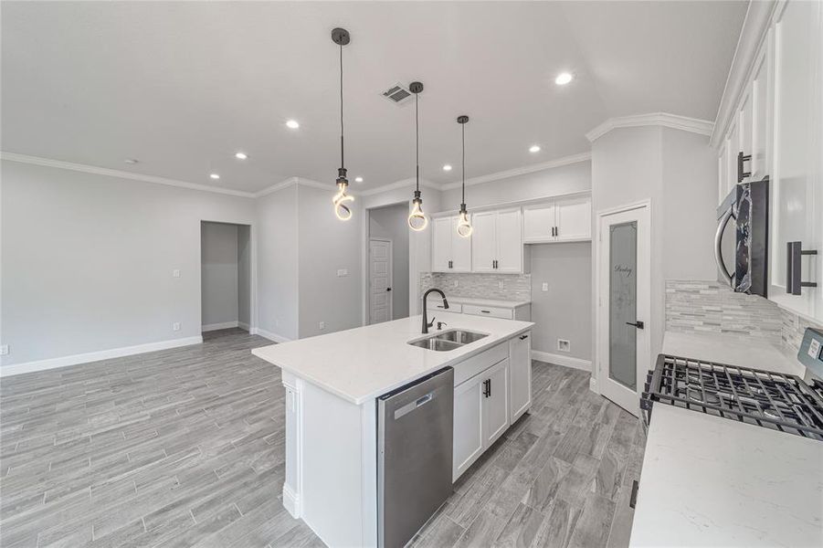 Kitchen with visible vents, appliances with stainless steel finishes, white cabinetry, a sink, and an island with sink