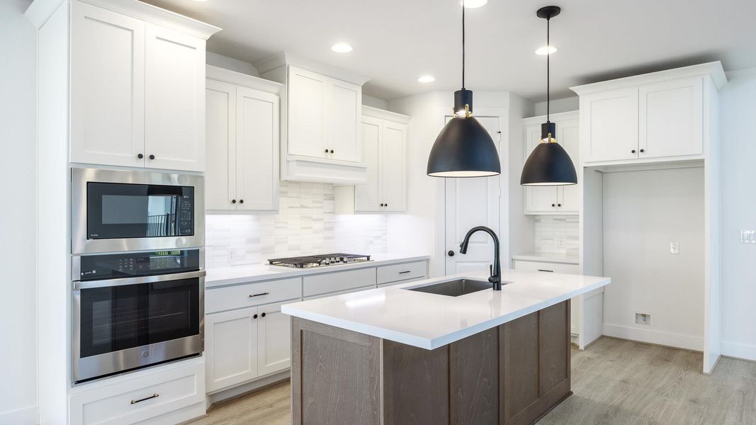 Kitchen featuring decorative backsplash, stainless steel appliances, a kitchen island with sink, white cabinetry, and light wood-type flooring Kitchen featuring decorative backsplash, stainless steel appliances, a kitchen island with sink, white cabinetry, and light wood-type flooring