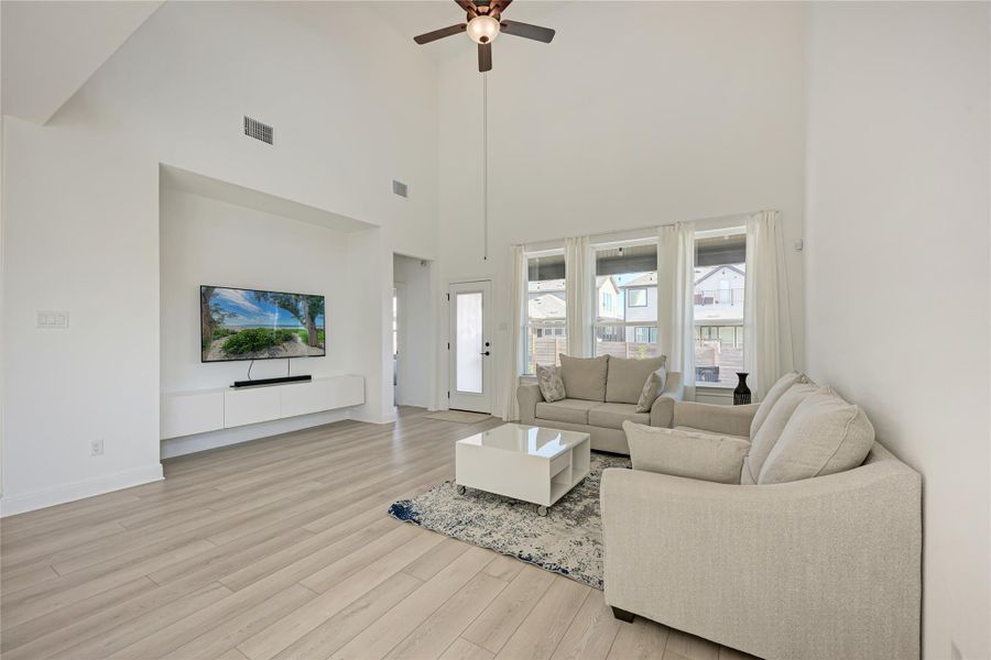 Living area featuring high vaulted ceilings, light wood-finish flooring, recessed lighting, and a prominent media wall with built-in cabinetry