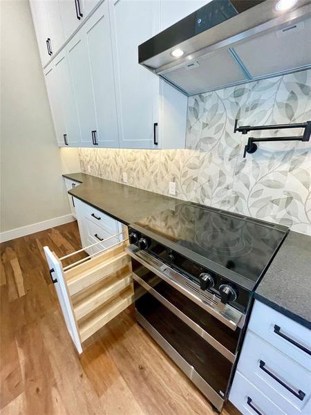 Kitchen featuring range hood, double oven range, light wood-style flooring, white cabinets, and dark stone countertops