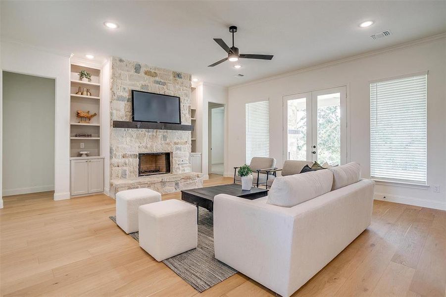 Living room featuring built in shelves, a stone fireplace, light hardwood / wood-style flooring, and ceiling fan