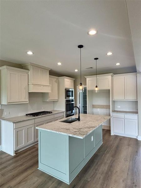 Kitchen featuring light stone counters, dark wood-style flooring, white cabinetry, an island with sink, and pendant lighting