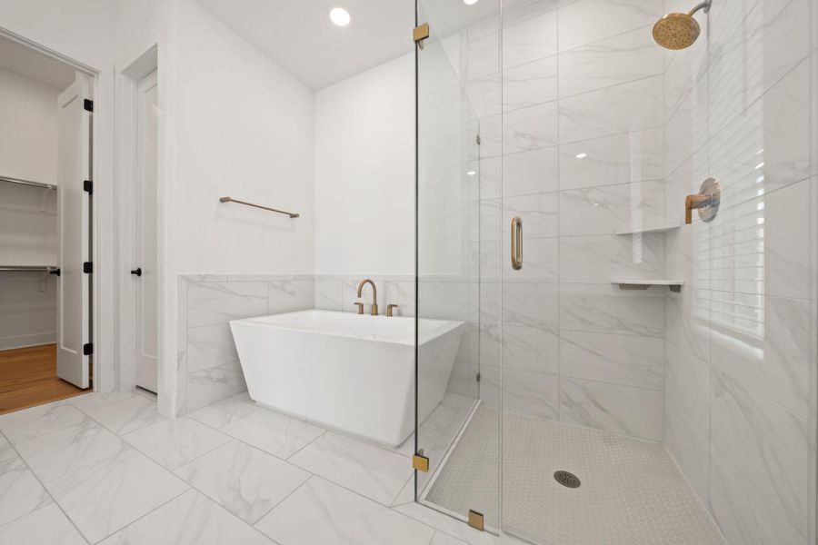 Full bath featuring tile walls, a soaking tub, a stall shower, a spacious closet, and light marble finish flooring