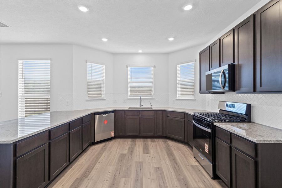 This spacious kitchen boasts high ceilings, Woodmont Dakota cabinets in a Smoke stain, Granite Summit White countertops, stainless steel Whirlpool appliances, a modern Daltile backsplash, recessed lighting, windows with blinds, an added breakfast bar to kitchen countertop, and a pantry—all overlooking the expansive Great Room. This spacious kitchen boasts high ceilings, Woodmont Dakota cabinets in a Smoke stain, Granite Summit White countertops, stainless steel Whirlpool appliances, a modern Daltile backsplash, recessed lighting, windows with blinds, an added breakfast bar to kitchen countertop, and a pantry—all overlooking the expansive Great Room.