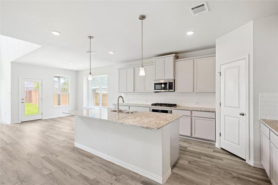 Kitchen with light wood-type flooring, an island with sink, backsplash, pendant lighting, and sink