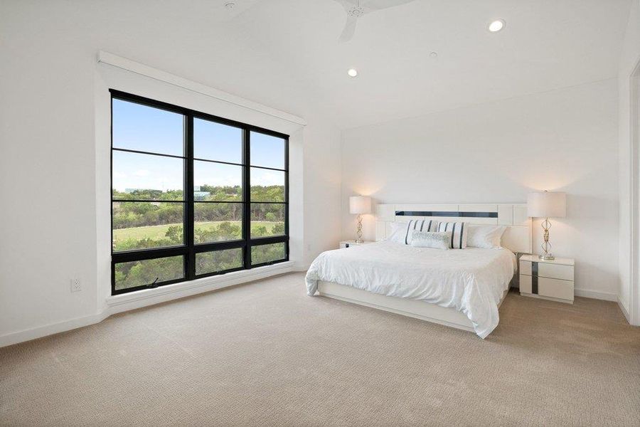 Spacious room featuring a large black-framed picture window overlooking a natural landscape, recessed ceiling lighting, a ceiling fan, and light-toned carpeting