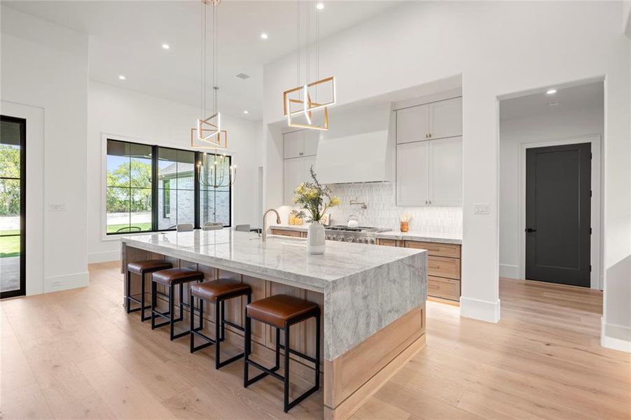 Kitchen with decorative backsplash, light stone counters, a breakfast bar area, a large island with sink, and light wood-style flooring