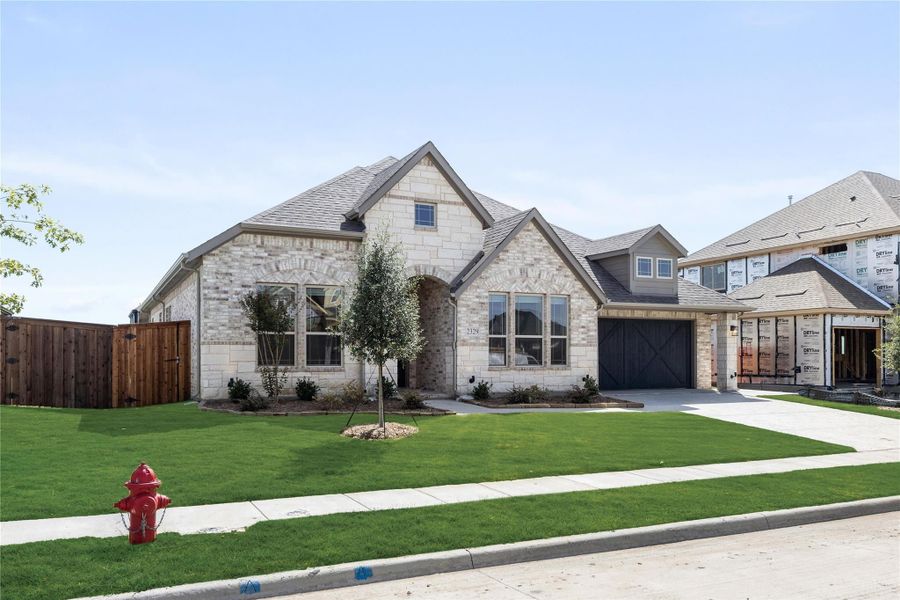 Single-story home with light stone exterior, arched entry, two-car garage, and green front lawn