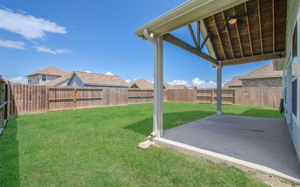 This photo showcases a spacious backyard with a well-maintained lawn and a covered patio area, enclosed by a wooden privacy fence, offering a perfect outdoor space for relaxation and entertainment.