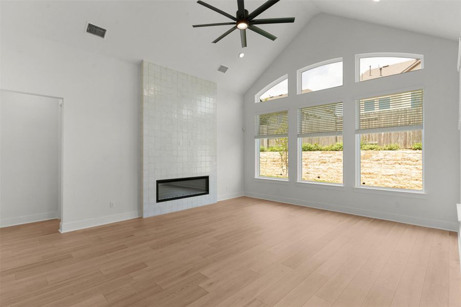 Vaulted ceiling living space featuring a linear fireplace with a textured tile surround, wood-finish flooring, and expansive windows Vaulted ceiling living space featuring a linear fireplace with a textured tile surround, wood-finish flooring, and expansive windows