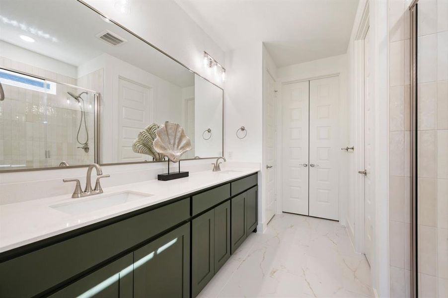 Bathroom featuring double vanity, light marble finish floors, a shower stall, and a closet