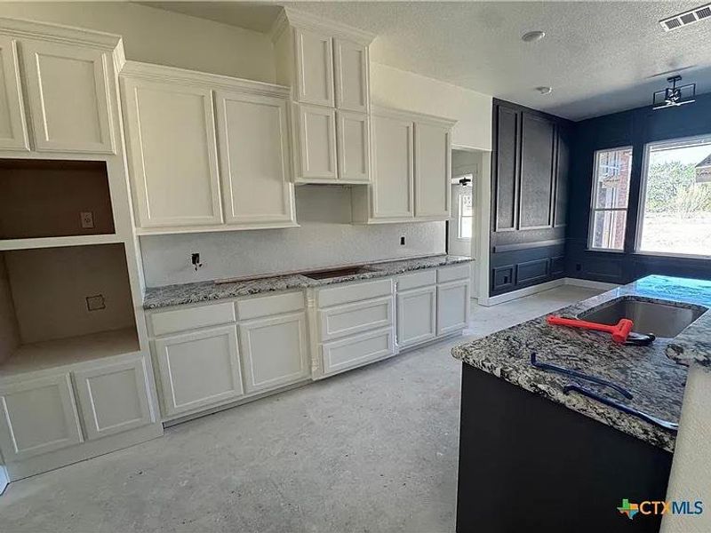 Kitchen featuring white cabinetry, a textured ceiling, visible vents, and light stone countertops