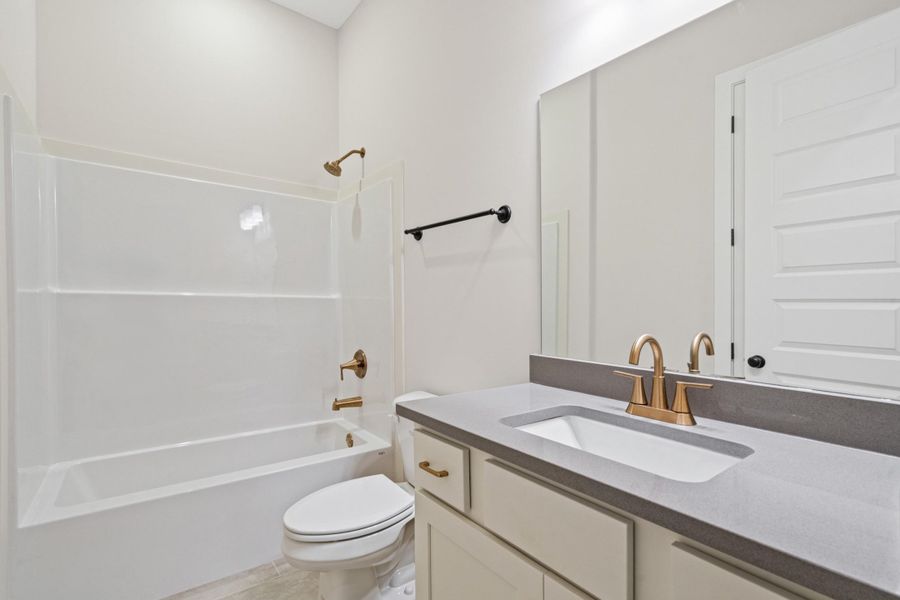 Bathroom featuring a white tub/shower combination with bronze fixtures, a vanity with a gray countertop and integrated sink, a bronze-finish faucet, and a large wall-mounted mirror Bathroom featuring a white tub/shower combination with bronze fixtures, a vanity with a gray countertop and integrated sink, a bronze-finish faucet, and a large wall-mounted mirror