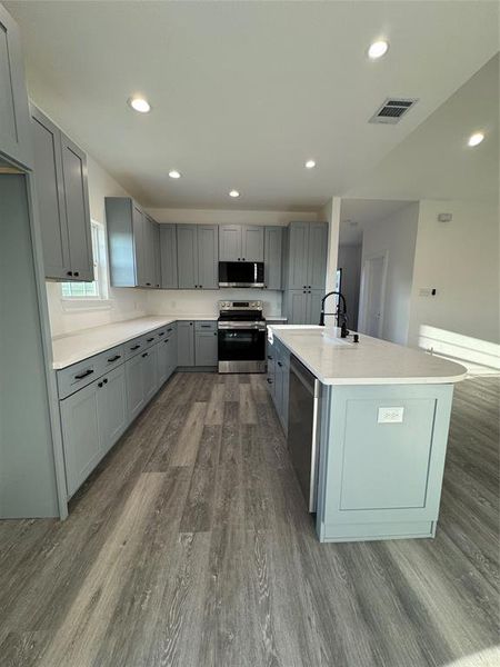 Kitchen featuring dishwashing machine, gray cabinets, stainless steel electric range oven, dark hardwood / wood-style floors, and an island with sink