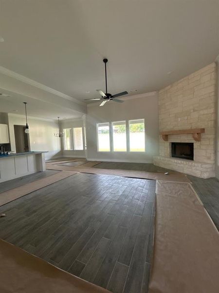 Expansive living area featuring a stone fireplace with a wood mantle, wood-look tile flooring, and a contemporary ceiling fan Expansive living area featuring a stone fireplace with a wood mantle, wood-look tile flooring, and a contemporary ceiling fan