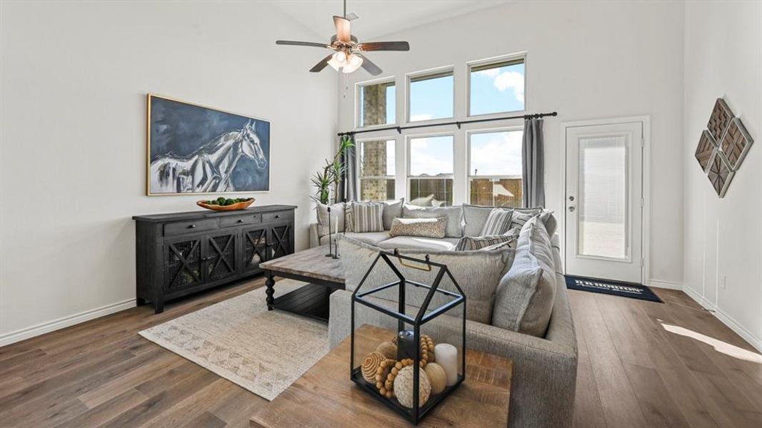 Spacious living area featuring high ceilings, wood-finish flooring, and multiple windows allowing abundant natural light Spacious living area featuring high ceilings, wood-finish flooring, and multiple windows allowing abundant natural light