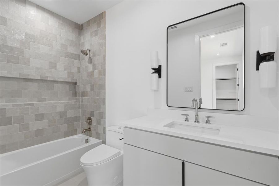 Modern bathroom featuring a built-in tub with tile surround and recessed niche, a toilet, a vanity with an integrated rectangular sink, and a rectangular mirror with black sconces