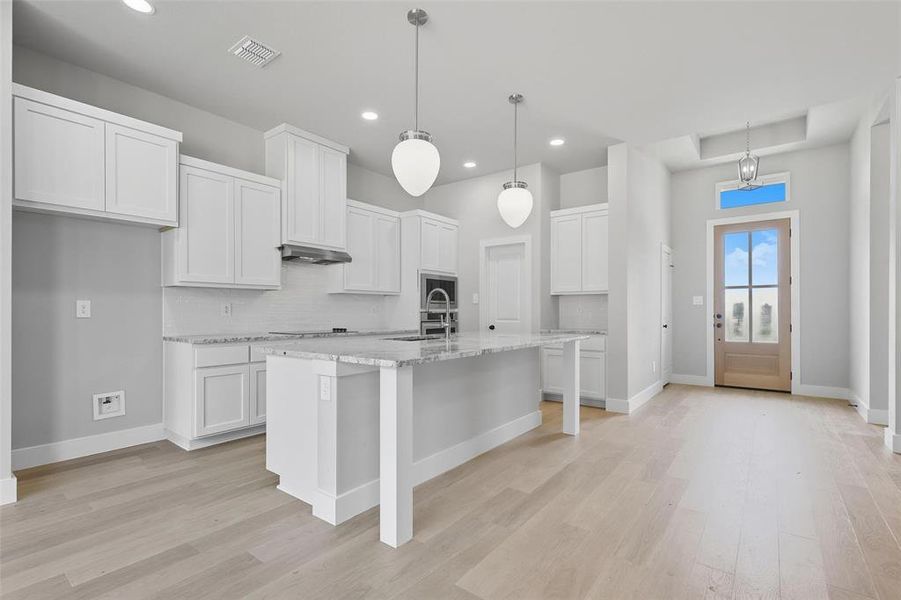 Kitchen featuring white cabinets, light stone counters, a kitchen island with sink, and light wood finished floors