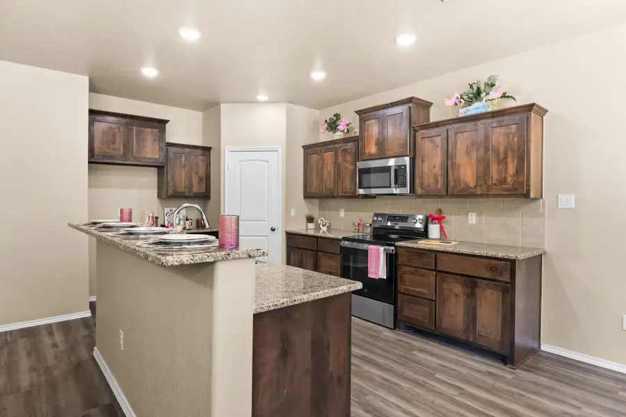 Kitchen with stainless steel appliances, dark brown cabinetry, dark wood-style floors, light stone countertops, and tasteful backsplash