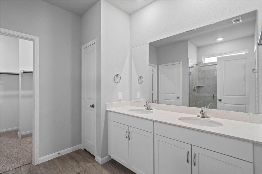 A bright and functional primary bath offering dual sinks for busy mornings, a large mirror, and a modern glass-enclosed shower, creating a serene and efficient space.