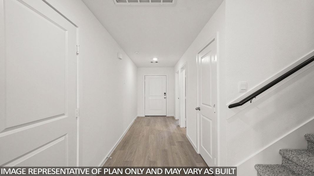 A well-lit entry hall with light wood flooring leads toward a white door.