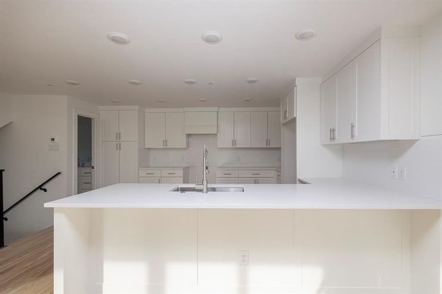 Kitchen with white cabinets, decorative backsplash, a peninsula, light countertops, and a sink