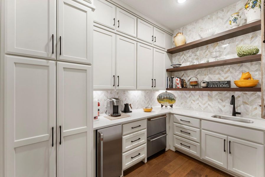 The butler’s pantry adds exceptional overflow storage and serving function just off the main kitchen. Full-height cabinetry, open shelving, under-cabinet lighting, an ice maker, refrigerator drawers, and a sink create a highly useful space for everyday organization and entertaining.