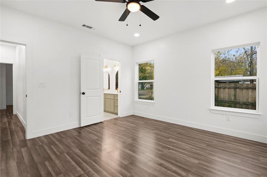 Unfurnished bedroom with multiple windows, ensuite bathroom, ceiling fan, and dark hardwood / wood-style floors