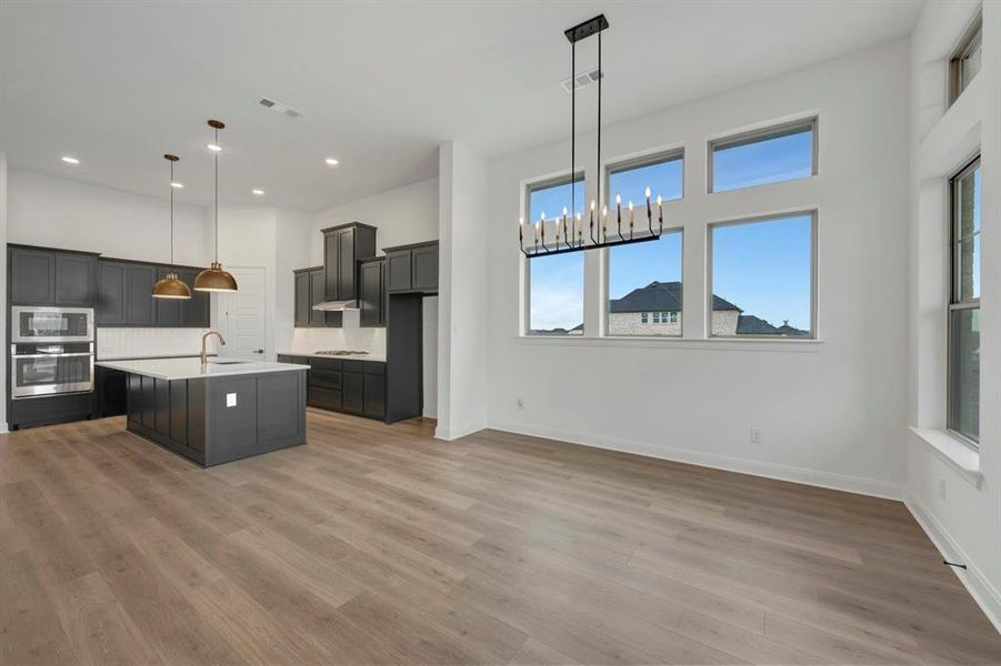Kitchen featuring a center island with sink, a chandelier, stainless steel appliances, light wood-style floors, and tasteful backsplash