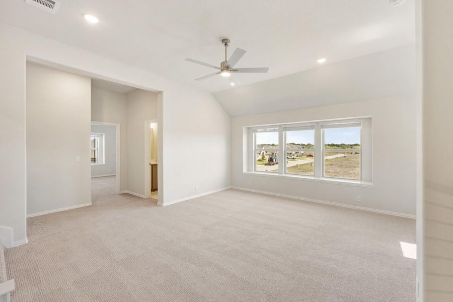 Spacious bedroom with vaulted ceiling, ceiling fan, carpet flooring, and large windows overlooking a neighborhood Spacious bedroom with vaulted ceiling, ceiling fan, carpet flooring, and large windows overlooking a neighborhood