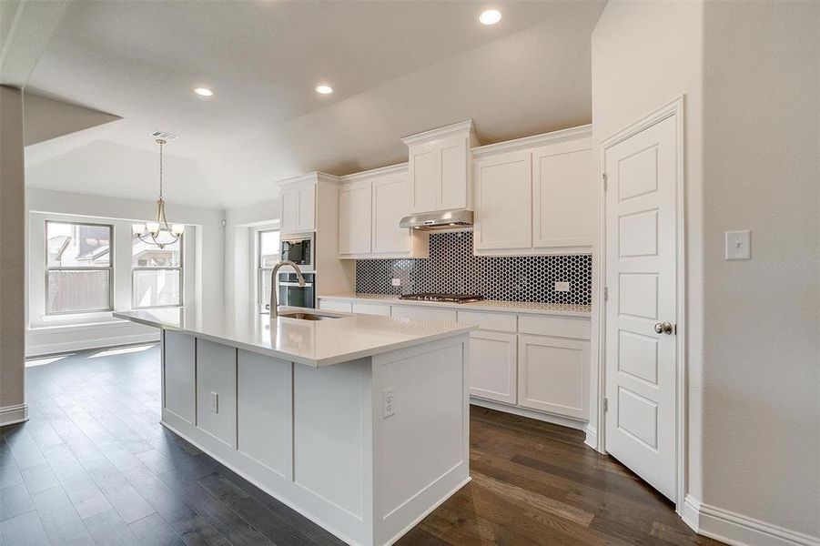 Kitchen featuring appliances with stainless steel finishes, white cabinetry, exhaust hood, a kitchen island with sink, and a chandelier