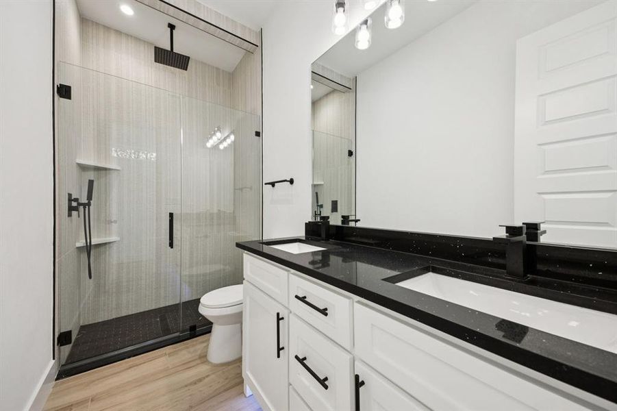 Full bath featuring double vanity, a shower stall, and light wood-style floors