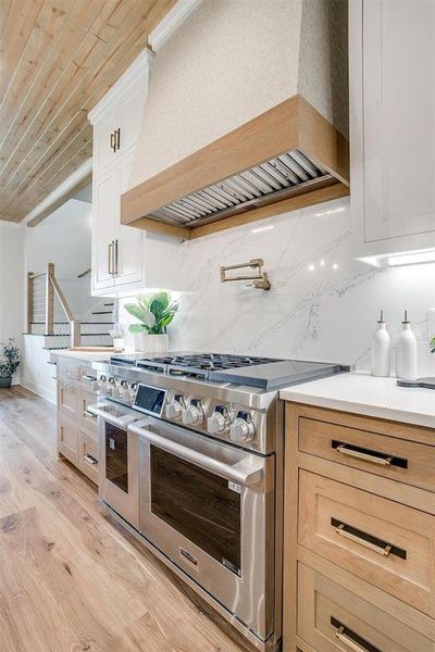 Kitchen with custom exhaust hood, double oven range, decorative backsplash, light wood finished floors, and wood ceiling