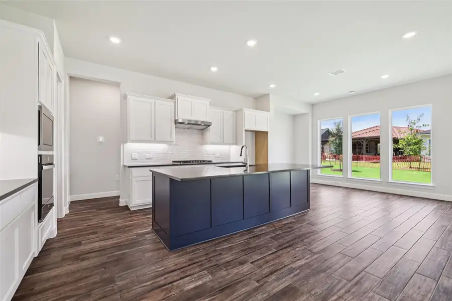 Kitchen with dark wood-type flooring, tasteful backsplash, white cabinetry, an island with sink, and recessed lighting