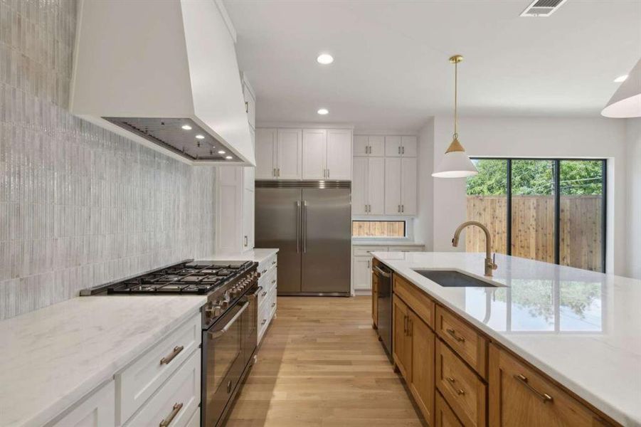 Kitchen featuring hanging light fixtures, white cabinets, light stone countertops, high quality appliances, and sink